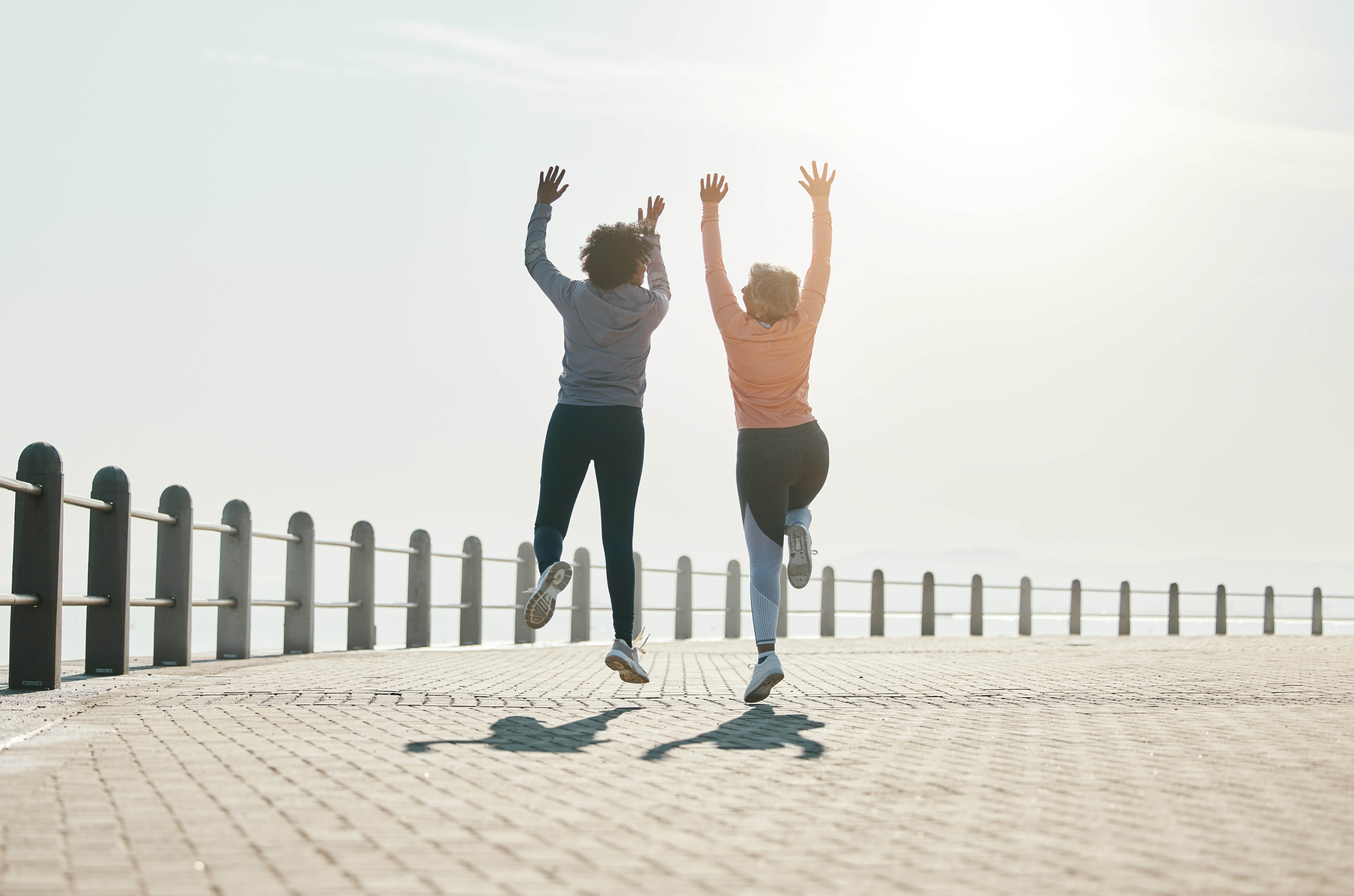 Two women jump off the ground in celebration, next to a fence around the water's edge